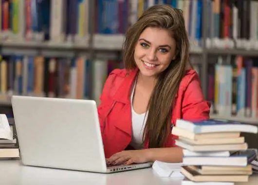 Une femme souriant dans une bibliothèque avec un ordinateur